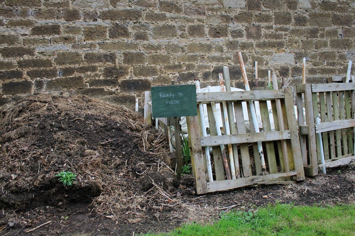 Compostbakken getimmerd uit oude paletten tegen een stenen muur